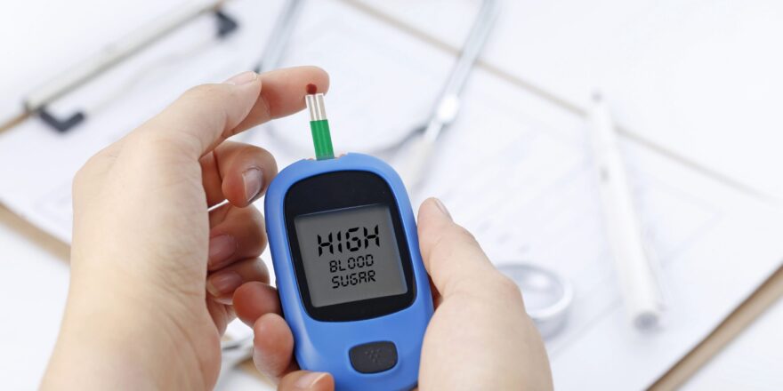 hand-holding-blood-glucose-meter-measuring-blood-sugar-background-is-stethoscope-chart-file-min
