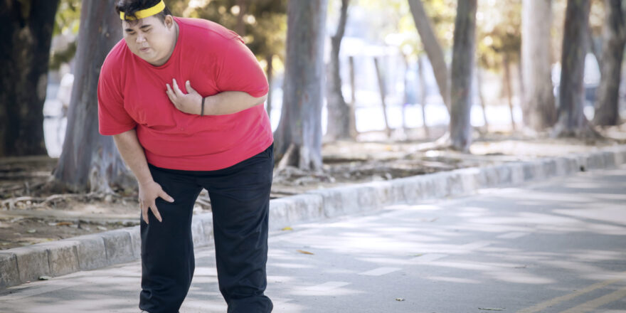 Picture of an overweight man having heart pain after running in the park at autumn time