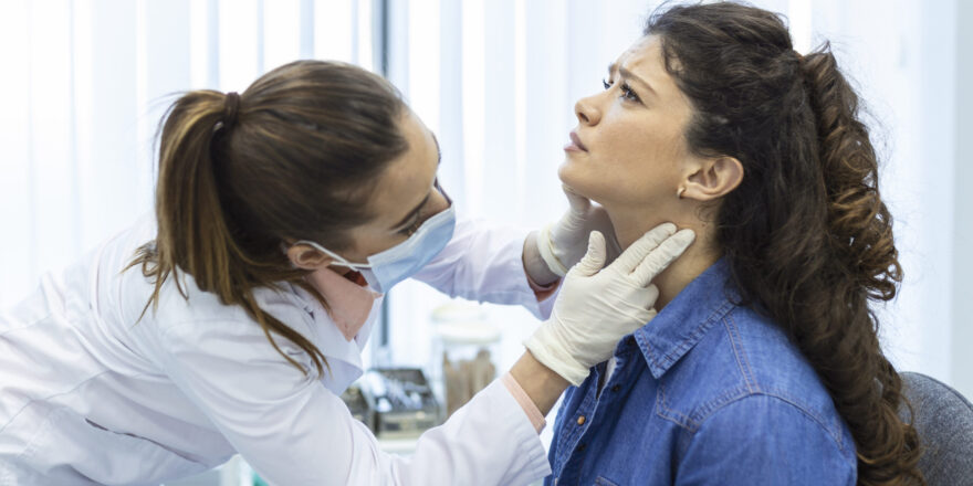 Endocrinologist examining throat of young woman in clinic. Women with thyroid gland test . Endocrinology, hormones and treatment. Inflammation of the sore throat